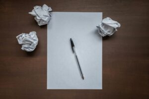 An empty sheet of paper, waiting to be written on, along with a biro and three screwed-up sheets of paper.