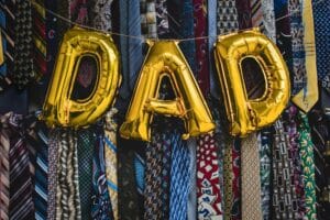 The word 'Dad' spelled out in balloon letters against a background of dress ties.
