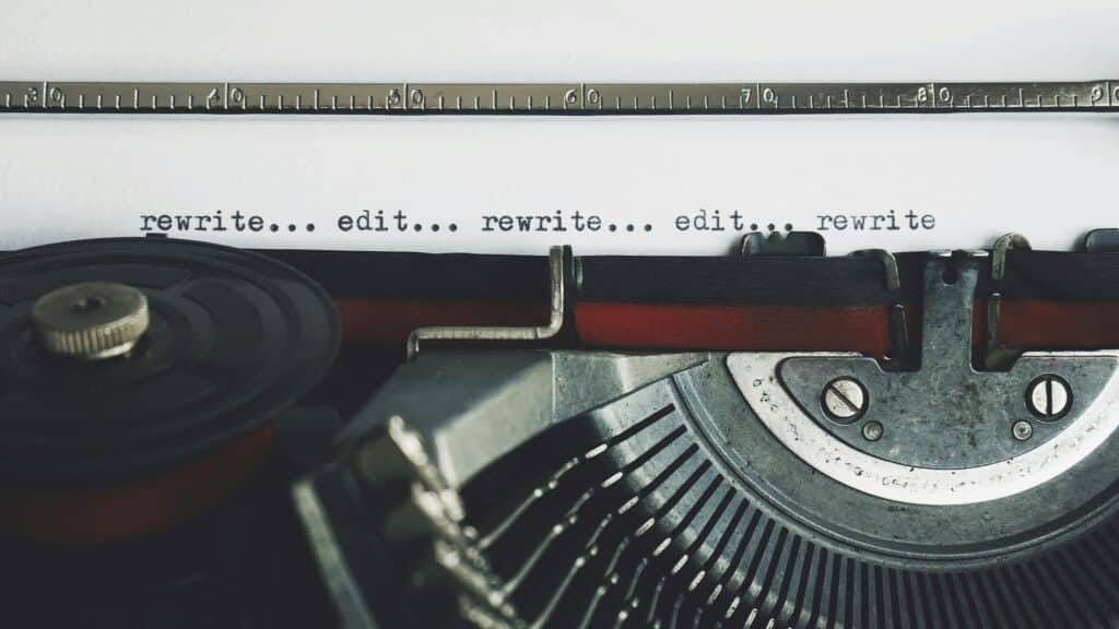 A close-up photograph of a typewriter, holding a sheet of paper displaying the words "rewrite...edit...rewrite...edit...rewrite"