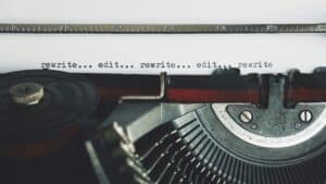 A close-up photograph of a typewriter, holding a sheet of paper displaying the words "rewrite...edit...rewrite...edit...rewrite"