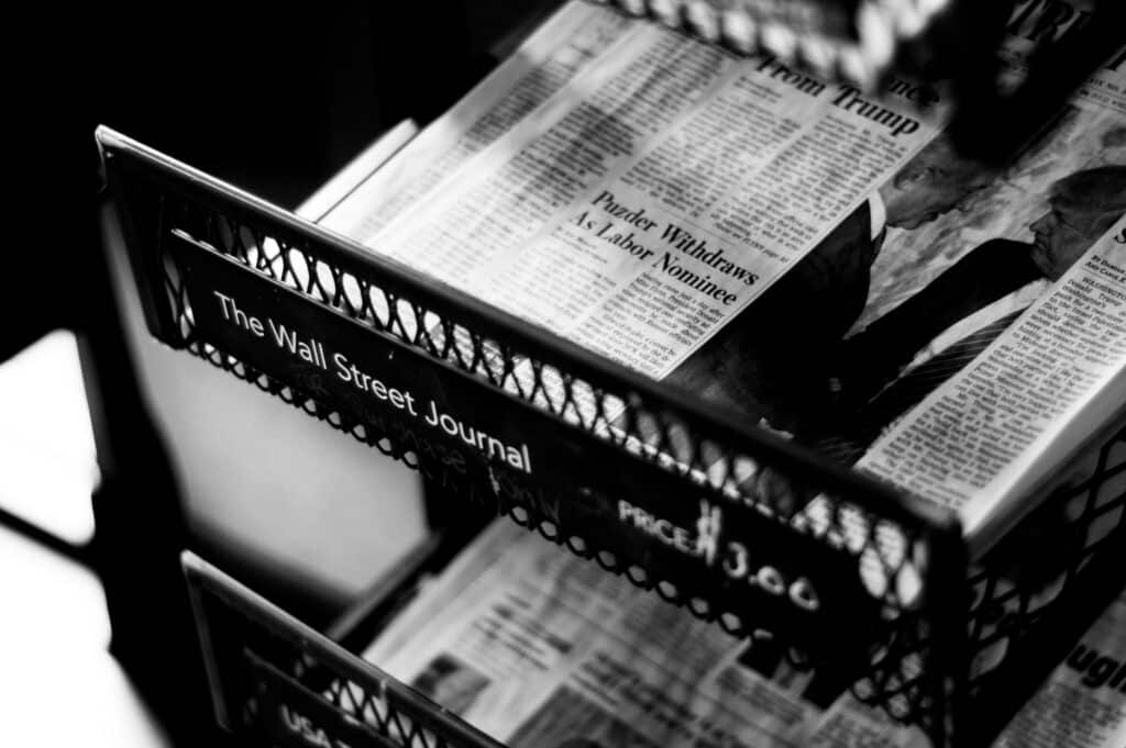 A black-and-white photograph of copies of The Wall Street Journal in a stand.
