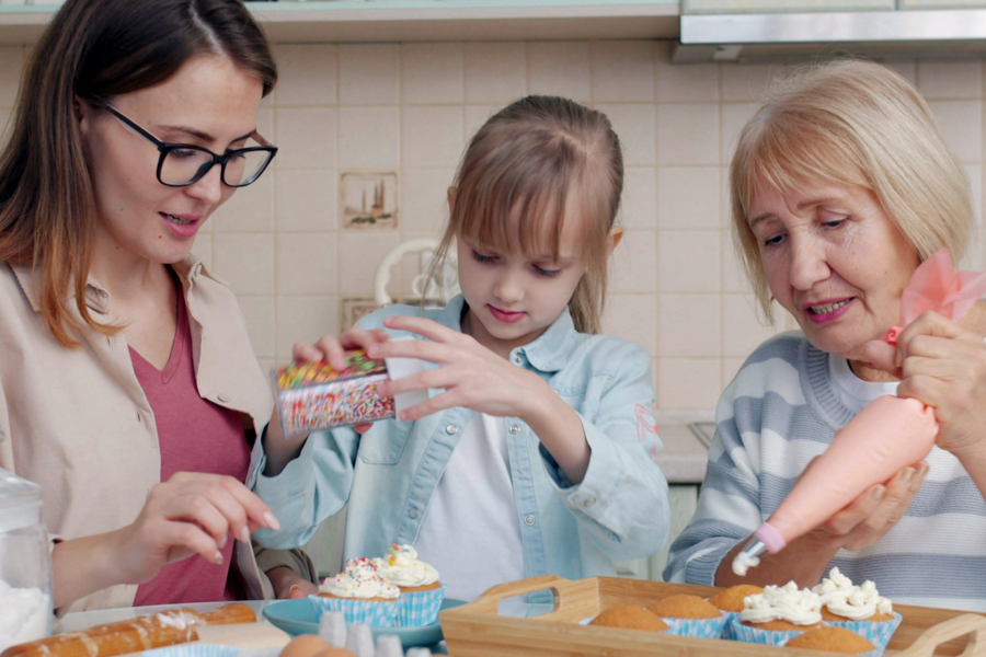 A photograph of three generations of female relations decorating cakes together.