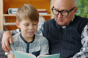 A young boy and an older man smiling together as they look at a book.