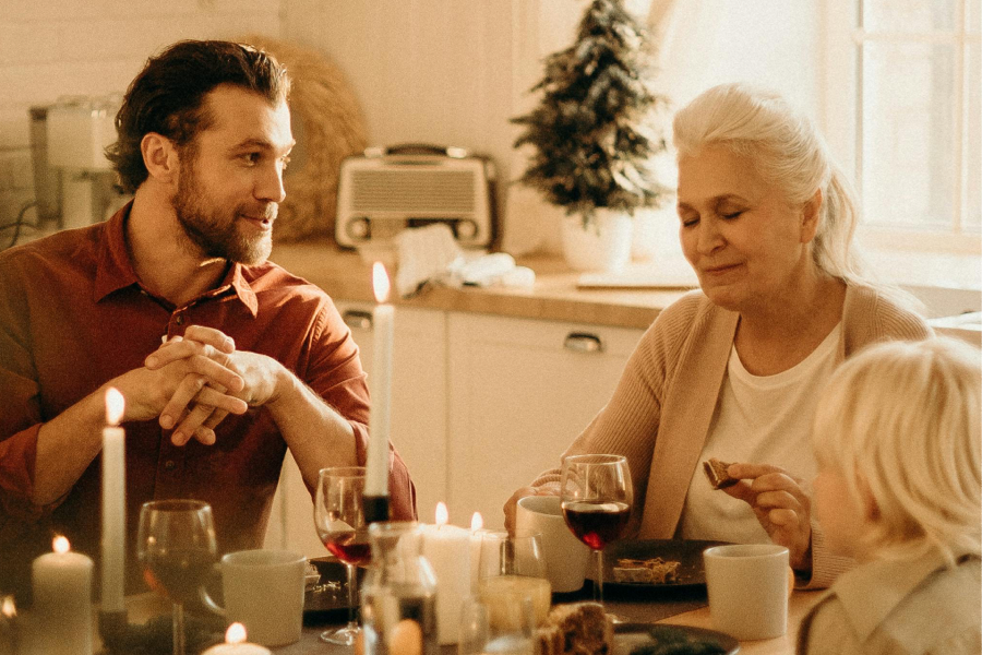 A younger man sitting at a table, talking with an older woman.
