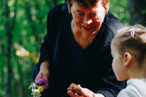 An older lady and a younger girl looking at flowers and shells together in a beautiful leafy glade!