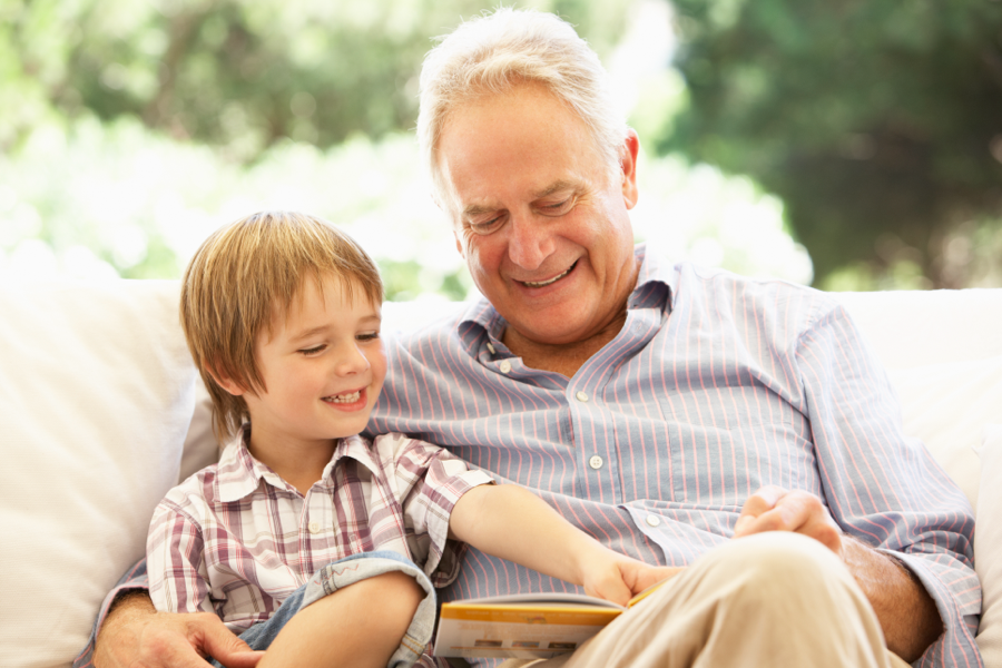 A young boy and an older man sitting together, laughing as they look at a book.