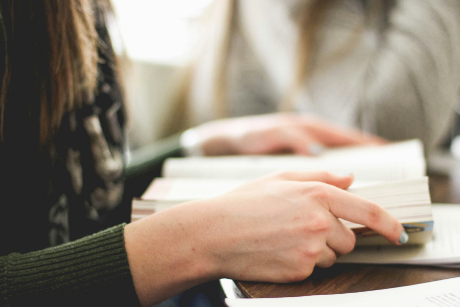 A close-up photograph of two hands holding a book open, flat.