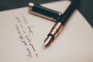 A photograph of a fountain pen laid to rest beside a page of handwriting.